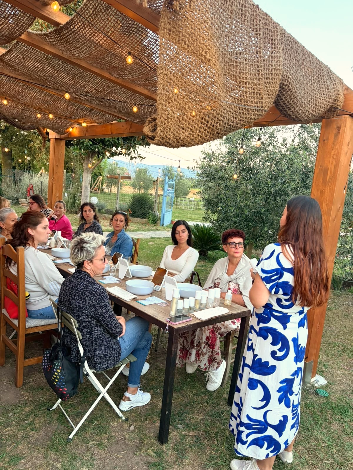 Donne sedute attorno alla tavola sotto il pergolato, mentre Dani racconta la serata